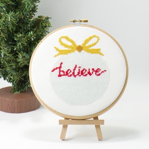 christmas believe ornament cross stitch pattern with red words and gold bow
