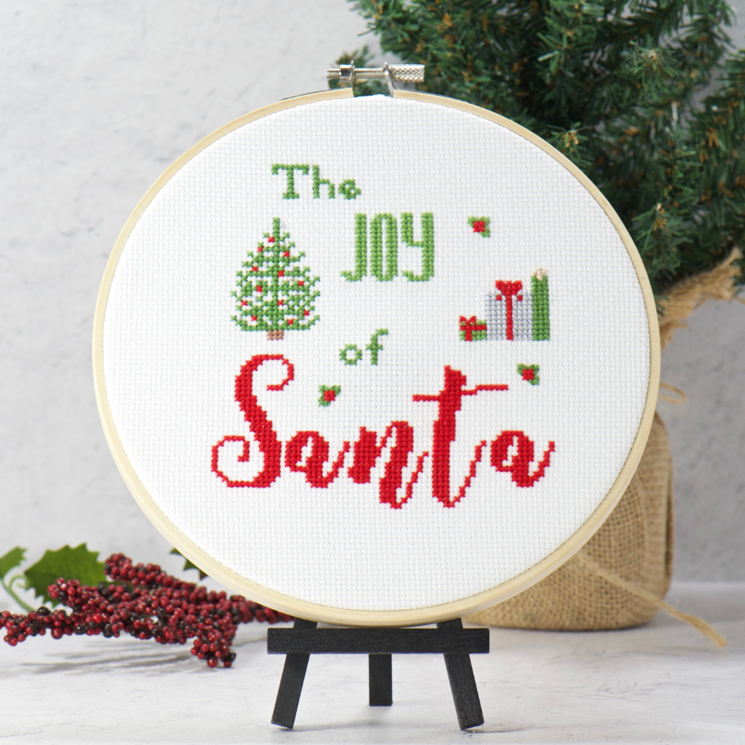 counted cross stitch kit with words the joy of santa among christmas tree and gifts