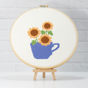 yellow sunny sunflowers in a blue cross stitch teacup on white 14 count fabric inside wood embroidery hoop