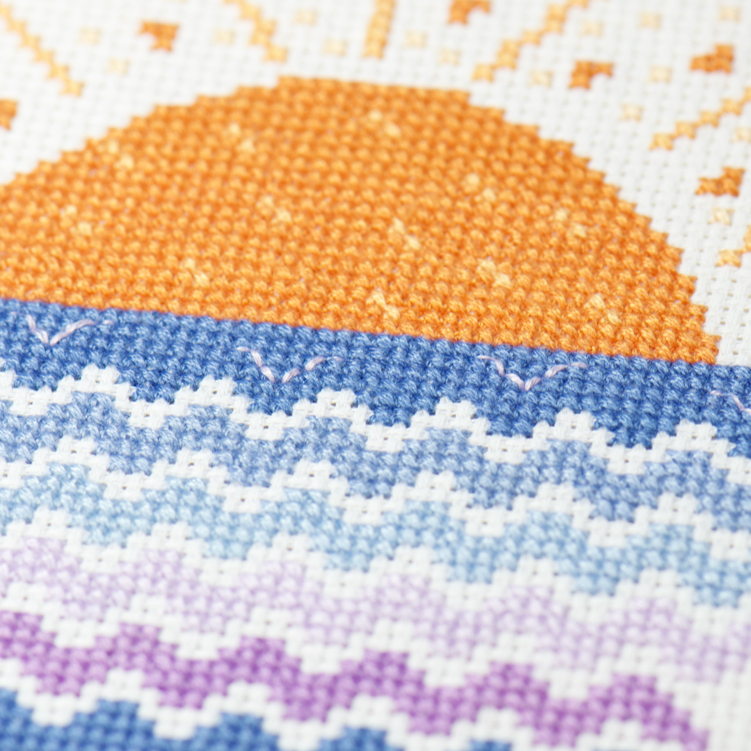 orange cross stitch sun rising from purple and blue counted embroidery waves