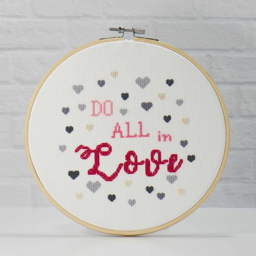 do all in love inspiring words in pink and rose with grey and beige hearts surrounding in this cross stitch hoop