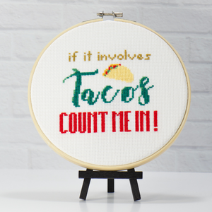 words if it involves tacos count me in with a yellow cross stitch taco on cross stitch fabric inside wood embroidery hoop
