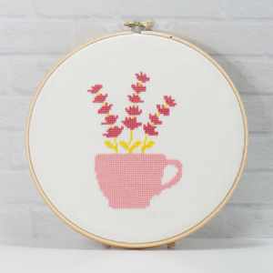 sweet pea flower in a teacup cross stitch in an embroidery hoop